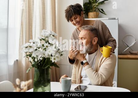 Un couple de seniors partage un moment chaleureux autour d’un café dans leur cuisine ensoleillée, entourée de fleurs. Banque D'Images