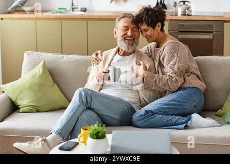 Couple profite d'un moment joyeux ensemble, sirotant du thé dans leur espace de vie confortable. Banque D'Images