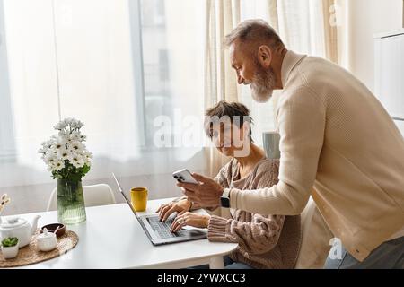 Couple mature apprécie la compagnie de l'autre avec un ordinateur portable et un téléphone dans leur maison confortable. Banque D'Images