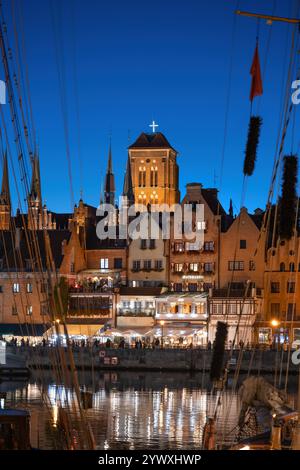 La vieille ville dans la ville de Gdansk la nuit en Pologne. Tour de l'église Sainte-Marie au-dessus des maisons à pignons historiques entre les mâts des voiliers à la rivière mari Banque D'Images