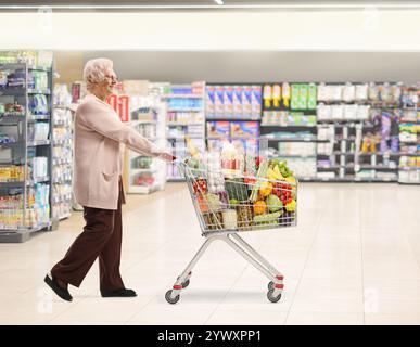 Photo de profil pleine longueur d'une dame senior marchant et poussant un chariot dans un supermarché Banque D'Images