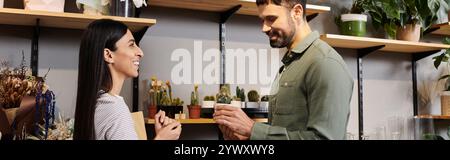 Un fleuriste qualifié s'engage avec un client masculin dans un magasin de fleurs vibrant rempli de verdure. Banque D'Images