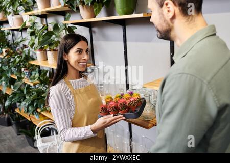 Beau fleuriste s'engage avec un client masculin tout en mettant en valeur des plantes colorées dans la boutique. Banque D'Images