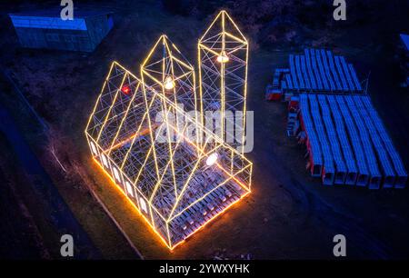 Fahrbinde, Allemagne. 12 décembre 2024. L'église de Noël érigée par des échafaudages ces derniers jours et illuminée de lumières de fées brille à la périphérie du village. (Vue aérienne avec un drone) L'échafaudage érigé avec deux tours d'environ 24 mètres de haut est maintenant la septième église de Noël. La construction précisément prévue sur l'autoroute entre Berlin et Hambourg s'allumera tous les soirs jusqu'à la fin du mois de janvier. Crédit : Jens Büttner/dpa/Alamy Live News Banque D'Images