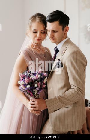 marié en costume beige et mariée en robe serrée de mariage lavande dans un studio lumineux Banque D'Images