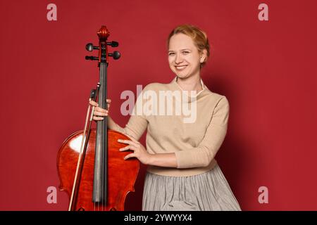 Belle jeune femme avec violoncelle sur fond rouge Banque D'Images