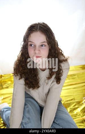 Adolescente assise sur la feuille d'or Survivial couverture crèmes cheveux bouclés pull Banque D'Images