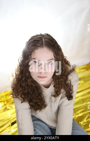 Adolescente assise sur la feuille d'or Survivial couverture crèmes cheveux bouclés pull Banque D'Images