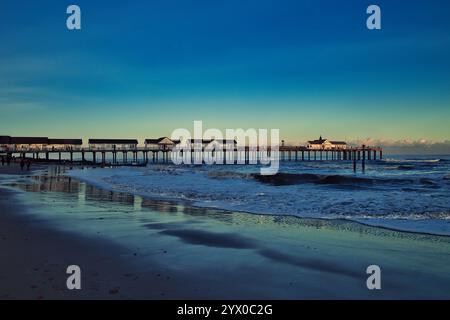 Southwold, Suffolk, Angleterre, Royaume-Uni - regardant le long de la plage de Southwold vers la jetée au coucher du soleil avec des vagues se brisant sur le bord de mer autour de la jetée Banque D'Images