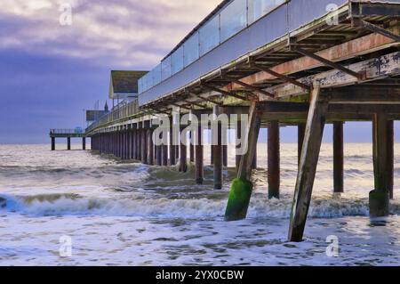 Southwold, Suffolk, Angleterre, Royaume-Uni - regardant sous la jetée Southwold au lever du soleil avec des vagues se brisant autour des supports de jetée en bois Banque D'Images