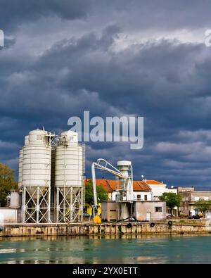 Des silos pour le stockage dans le port fluvial industriel avec des nuages au-dessus. Banque D'Images