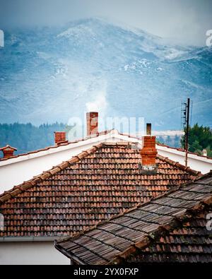 Toits avec fumeurs cheminées et collines enneigées à l'arrière. Banque D'Images