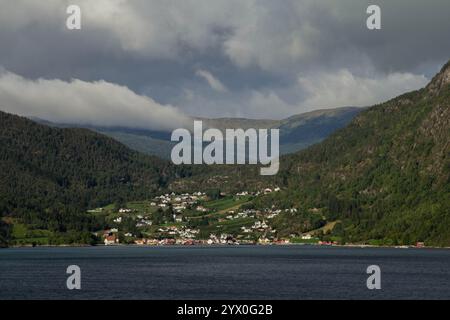 Un village pittoresque niché au bord d'un fjord, vu de l'eau. L'image montre les eaux paisibles au premier plan Banque D'Images