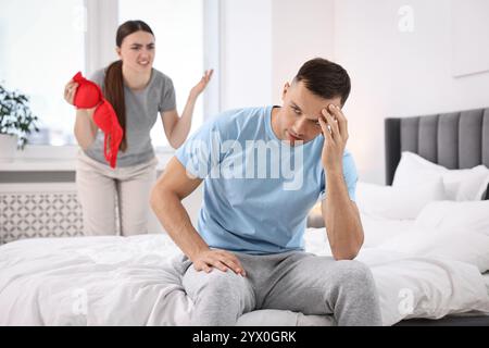 Angry Wife montrant le soutien-gorge de maîtresse comme preuve à son mari infidèle alors qu'il l'ignore dans la chambre, focus sélectif Banque D'Images