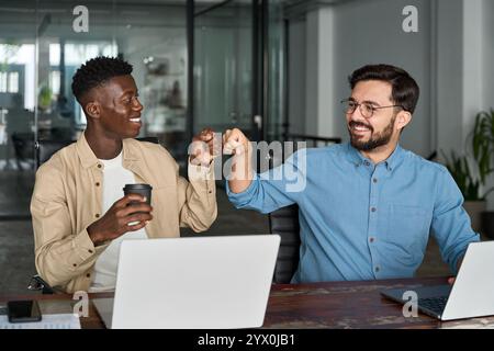 Deux employés masculins professionnels heureux et diversifiés donnent coup de poing au travail. Banque D'Images