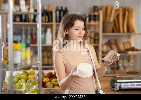 Jeune cliente féminine choisissant le fromage emballé dans l'épicerie Banque D'Images