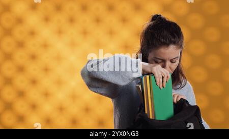 Portrait de femme fouillant à travers le sac à dos, prenant le livre, isolé sur fond de studio. Élève enlevant le manuel utilisé à des fins éducatives du sac à dos de l'école, appareil photo A. Banque D'Images