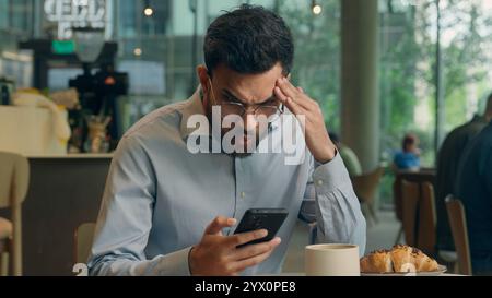 Homme d'affaires indien Guy homme d'affaires arabe homme d'affaires visiteur homme dans le café espère tenir le téléphone portable recevoir de mauvaises nouvelles message escroquerie téléphone portable échec Banque D'Images