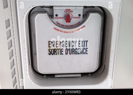 Gros plan d'une trappe de sortie de secours sur le toit d'un autobus avec un autocollant bilingue indiquant « sortie de secours. Sortie D'urgence' et un verrou rouge. Banque D'Images