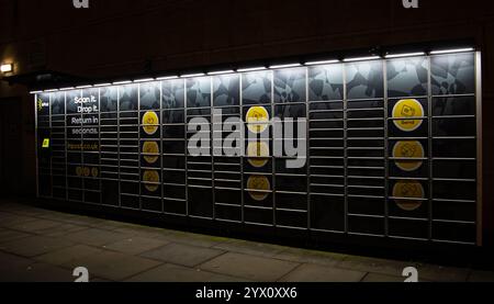 Un mur de casier à colis sombre et éclairé sur une rue avec des cercles jaunes marqués et des instructions textuelles pour numériser et déposer Banque D'Images
