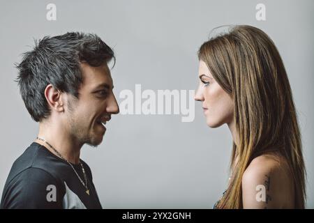 Profil d'un jeune couple engagé dans une discussion en face à face, avec l'homme souriant et la femme affichant une expression sérieuse, capturant les dix Banque D'Images