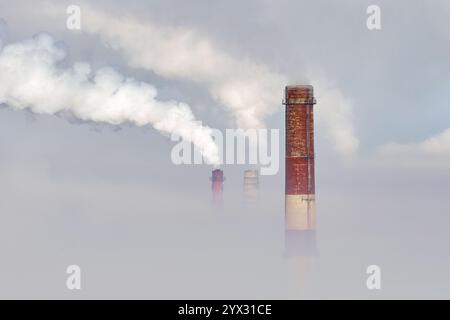 Visibilité obscurcie par un épais brouillard lorsque de la fumée s'écoule des cheminées industrielles dans une zone de fabrication à l'aube Banque D'Images