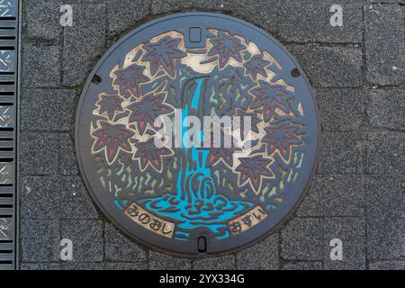 Un design coloré de couvercle de trou d'homme avec cascade et feuilles d'érable d'automne dans la ville de Minoh, Osaka, Japon. Traduction : approvisionnement en eau de la ville de Minoh. Banque D'Images