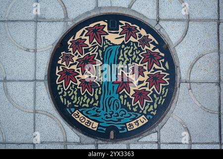 Un design coloré de couvercle de trou d'homme avec cascade et feuilles d'érable d'automne dans la ville de Minoh, Osaka, Japon. Traduction : approvisionnement en eau de la ville de Minoh. Banque D'Images