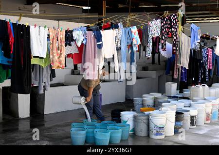 Reynosa, Mexique. 11 décembre 2024. Un migrant verse de l'eau dans un seau dans un abri dans la ville frontalière de Reynosa, Tamaulipas, Mexique, 11 décembre 2024. Reynosa, une ville frontalière de Tamaulipas, se trouve de l'autre côté du Rio Grande de McAllen, Texas des États-Unis. En raison de sa situation géographique, Reynosa sert de porte d'entrée majeure pour les migrants d'Amérique centrale et d'autres régions qui tentent d'entrer aux États-Unis. Les refuges de cette région fournissent un logement temporaire aux migrants en attente de demandes d'asile, de permis de transit ou de retour dans leur foyer. Crédit : Li Muzi/Xinhua/Alamy Live News Banque D'Images