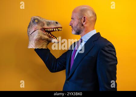 Un homme portant un masque de dinosaure dans sa main sur un fond jaune. Banque D'Images