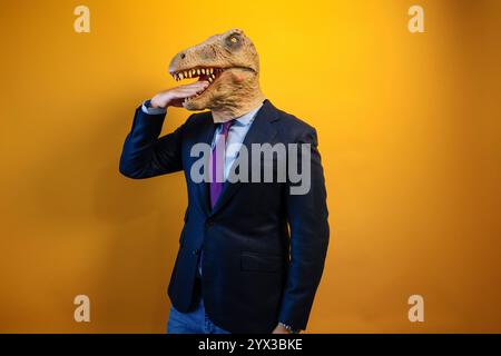 Un homme portant un masque de dinosaure se mord la main. Banque D'Images