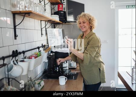 Femme d'âge moyen souriante faisant du café dans la cuisine. Banque D'Images