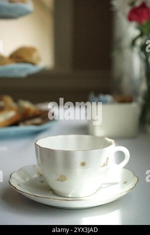 Tasse à thé en porcelaine blanche sur table avec des pâtisseries en arrière-plan Banque D'Images