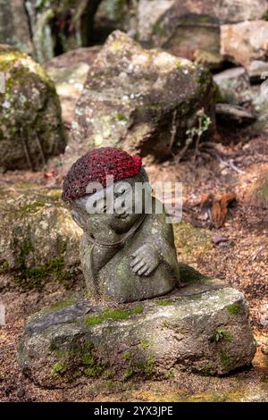 Une statue de bébé bouddha portant une casquette rouge dans la forêt. Banque D'Images