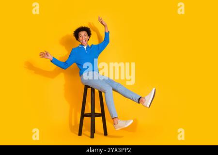 Photo pleine longueur du beau jeune homme excité chaise en bois assis ludique habillé élégant vêtement bleu isolé sur fond de couleur jaune Banque D'Images