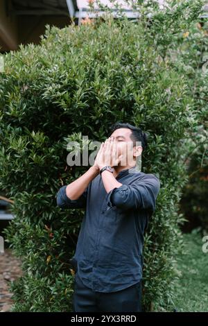 Un homme d'Asie du Sud-est éternuant, capturé dans un moment naturel. Idéal pour la santé, le style de vie ou les projets sur le thème des allergies mettant en valeur les réactions quotidiennes et Banque D'Images
