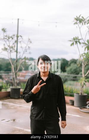 Un homme d'Asie du Sud-est faisant un signe de paix avec ses doigts, symbolisant l'harmonie et la positivité. Parfait pour le style de vie, la paix, ou l'expression joyeuse Banque D'Images