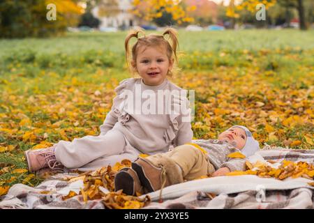 Jolie petite fille de 3 ans assise à côté de son nouveau-né petit frère. Famille heureuse sur un pique-nique dans un parc d'automne parmi les feuilles jaunes. À l'extérieur Banque D'Images