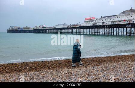 Brighton UK 13 décembre 2024 - Un marcheur sur la plage de Brighton près de la jetée par une journée froide et grise le long de la côte sud : crédit Simon Dack / Alamy Live News Banque D'Images