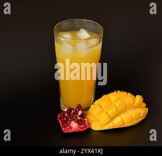 Un grand verre d'un mélange de jus de fruits avec de la glace sur un fond noir, avec des morceaux de mangue mûre et de grenade mélangés. Gros plan. Banque D'Images