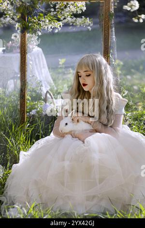 La belle fille avec lapin blanc dans le jardin fleuri de pommiers-arbres. Fleurs blanches dans un jardin ensoleillé. Pommiers de printemps en fleurs. Beaut Banque D'Images