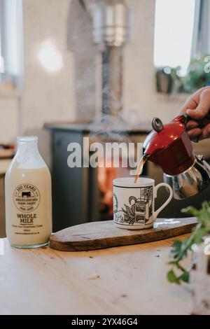 Une personne verse du café dans une tasse à côté d'une bouteille de lait entier. La scène est confortable et accueillante, avec l'arôme de remplissage de café fraîchement moulu Banque D'Images