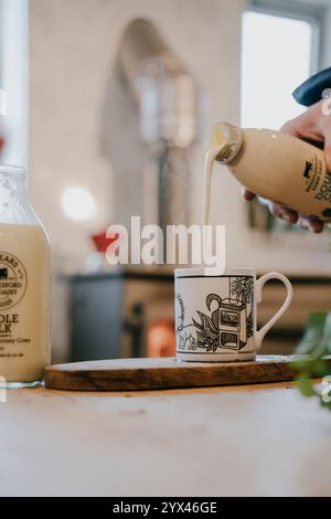 Une personne verse du lait dans une tasse blanche. Le lait provient d'une bouteille sur laquelle figure la mention « lait de vache » Banque D'Images