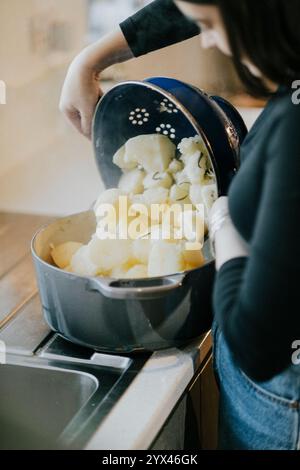 Une femme fait cuire des pommes de terre dans une grande casserole. Elle verse les pommes de terre dans une passoire Banque D'Images