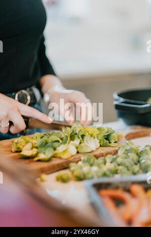 Une femme découpe des légumes sur une planche à découper. Les légumes comprennent le brocoli et les carottes. La femme porte une chemise noire et un Jean Banque D'Images