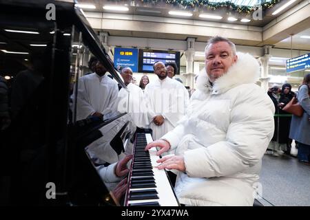 Tony Mortimer, ancien chanteur d'East 17, surprend les navetteurs de la station St Pancras International à Londres avec une performance pop-up de son numéro un de Noël 1994, « Stay Another Day », soutenu par le London Community Gospel Choir. La performance survient alors que Tony s'est associé à l'association de bienfaisance de musicothérapie Nordoff et Robbins pour célébrer le 30e anniversaire de la sortie de la chanson. Date de la photo : vendredi 13 décembre 2024. Banque D'Images