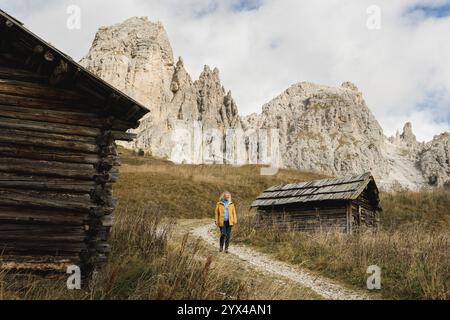 Femme en imperméable jaune randonnée dans les Alpes Dolomites avec des sommets rocheux sur le fond. Vieilles fermes en bois au premier plan. Banque D'Images