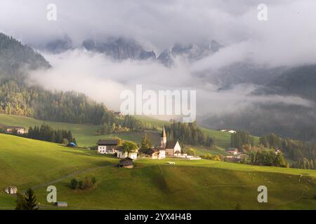Paysage nocturne nuageux de prairie alpine et montagne Seceda dans les Dolomites, Tyrol du Sud, Italie. Vieille église en pierre éclairée par la lumière du coucher du soleil. Banque D'Images