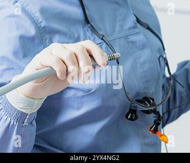 Dentiste portant des loupes chirurgicales et tenant une perceuse dentaire se préparant pour une intervention dentaire Banque D'Images