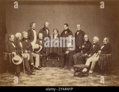 Le Friday Night Club, années 1870 Portrait de groupe de treize hommes assis et debout en demi-cercle avec une petite table drapée de tissu au sommet du demi-cercle. Quelques-uns des hommes tiennent des chapeaux ou des cannes. Banque D'Images